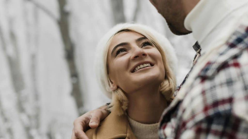 A smiling woman looking up at a man while standing close together outdoors.