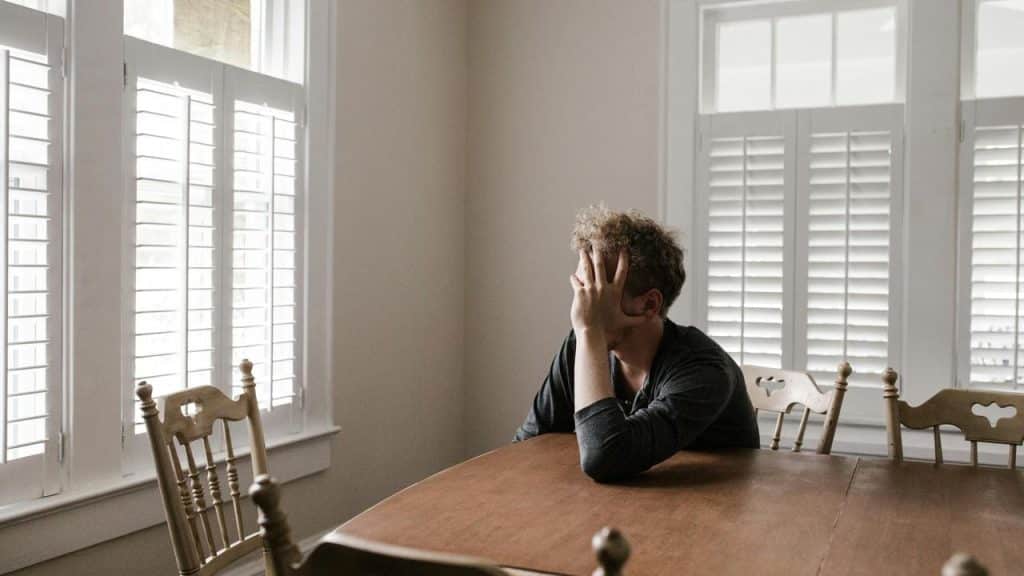 A man sitting at a table with his head in his hand near a window.
