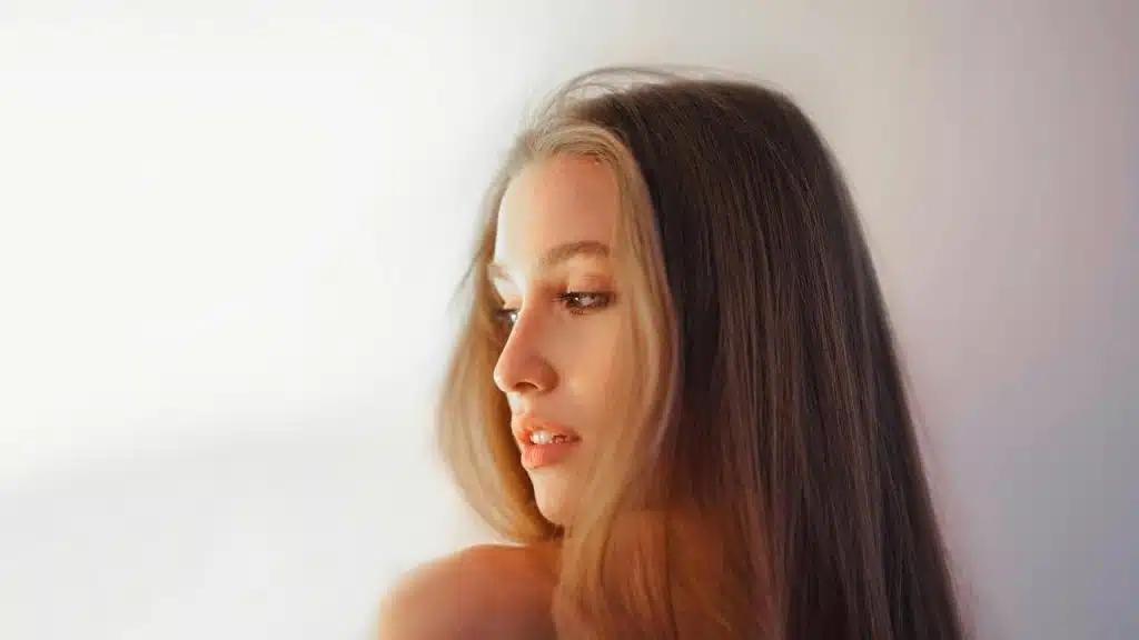 A woman with long hair looking to the side against a softly lit background.