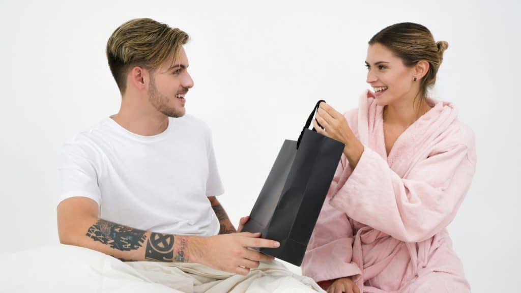 A man in a white shirt hands a shopping bag to a smiling woman.
