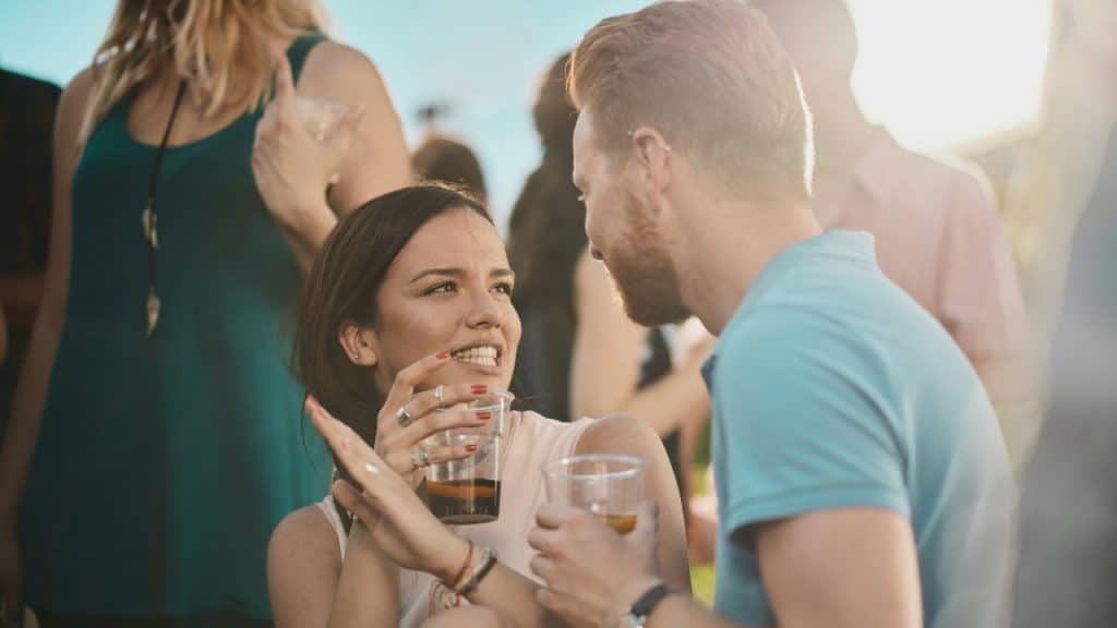 A woman talks to a man while holding a plastic cup at an outdoor event.