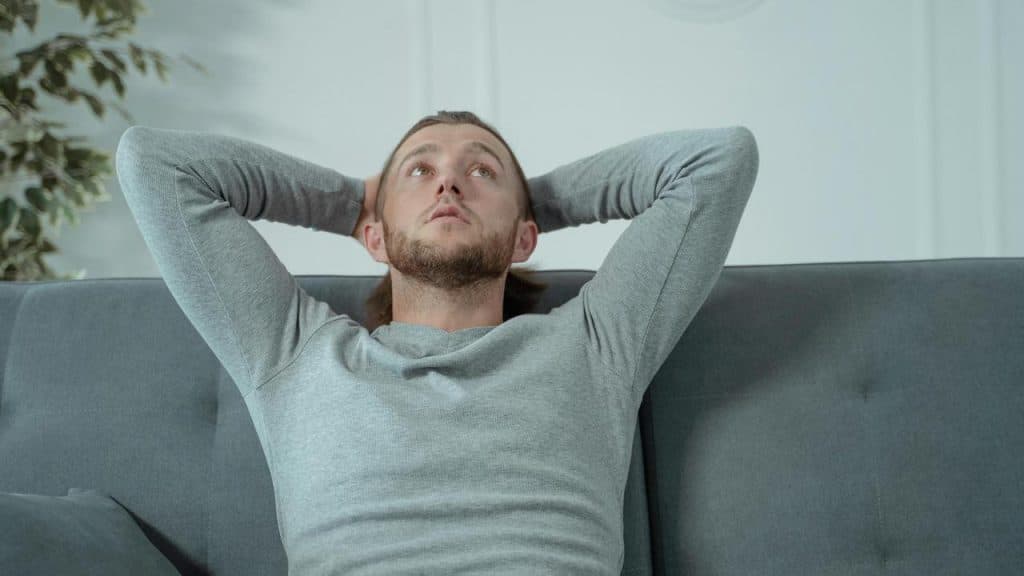 A man leaning back on a couch with his hands behind his head.