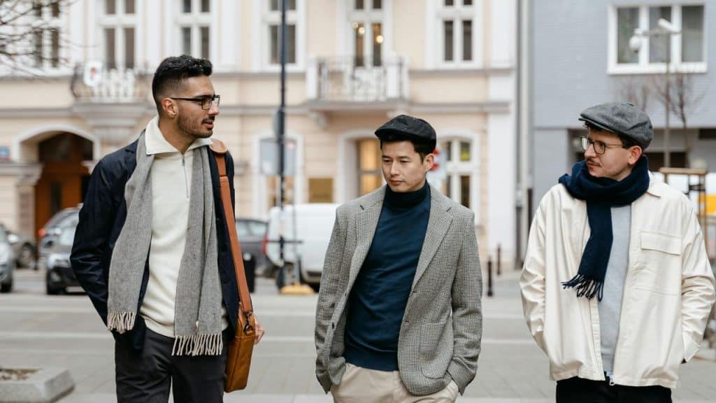 A group of three men walking and talking on a city street in coats and scarves.