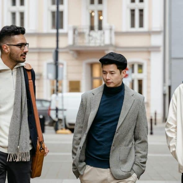 A group of three men walking and talking on a city street in coats and scarves.
