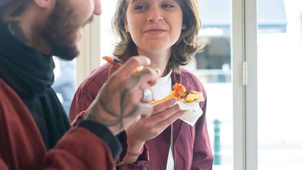 A man and woman eating pizza and talking indoors.