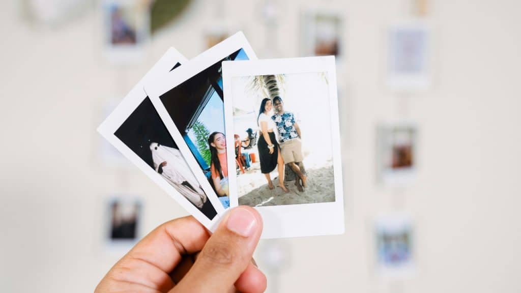 A hand holds up three instant film photographs showing different people and outdoor scenes.