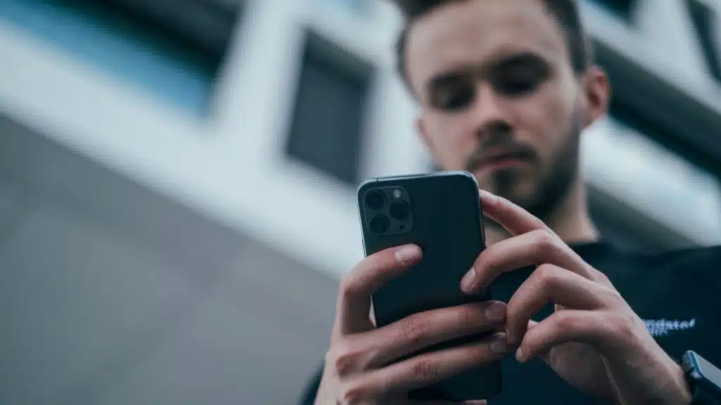 A man with a serious expression holds and looks down at his smartphone.