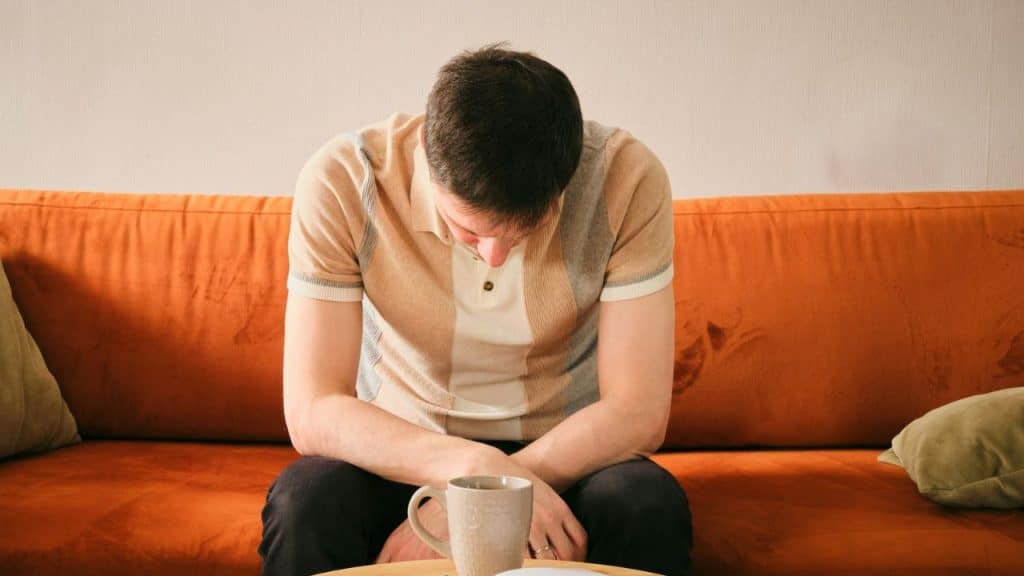 A person with their head bowed sits on an orange couch behind a mug.
