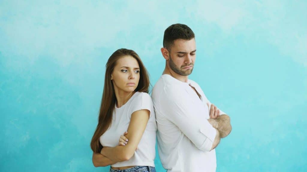 A couple standing with their backs to each other and looking upset.