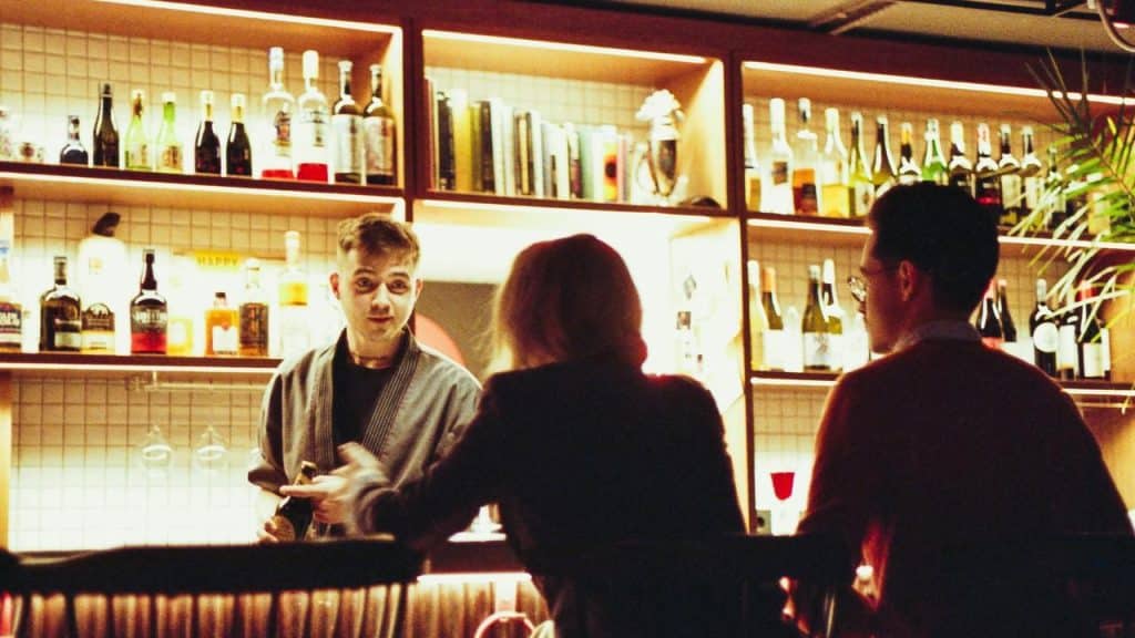 A bartender serving drinks to two customers at a bar.