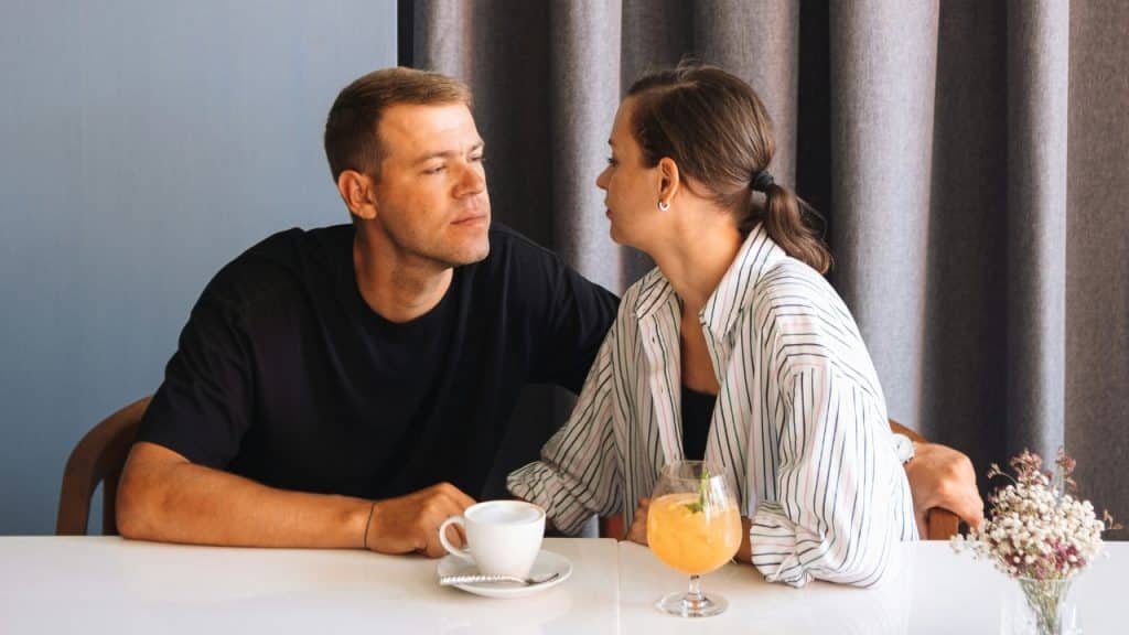 A man and woman sitting at a table with coffee and a cocktail, facing each other.
