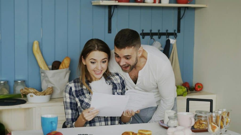 A man and woman look at papers together while sitting at a kitchen table.