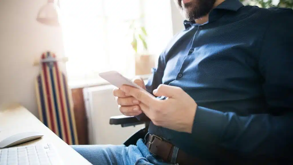 A man sitting at a desk looking at his phone.