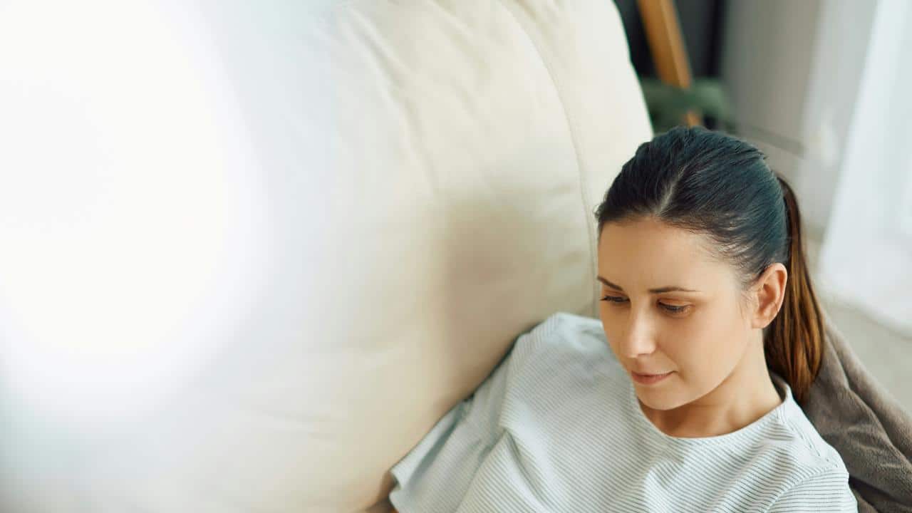 A woman sits on a couch looking down thoughtfully.