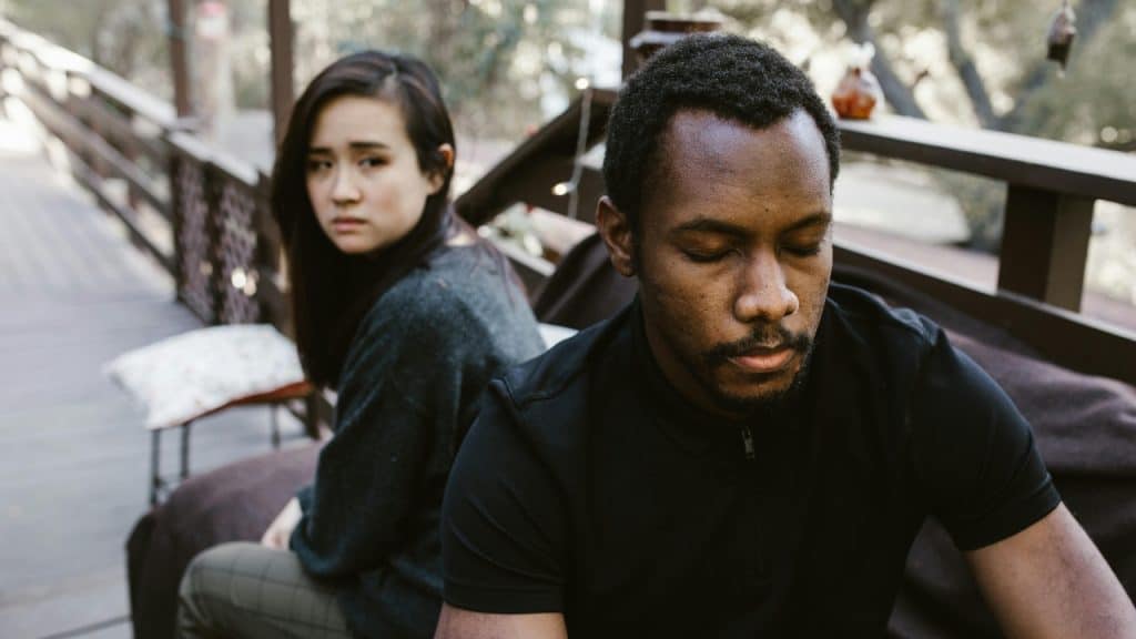A man with eyes closed and a woman looking back toward him on a wooden deck.