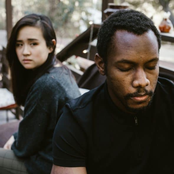 A man with eyes closed and a woman looking back toward him on a wooden deck.