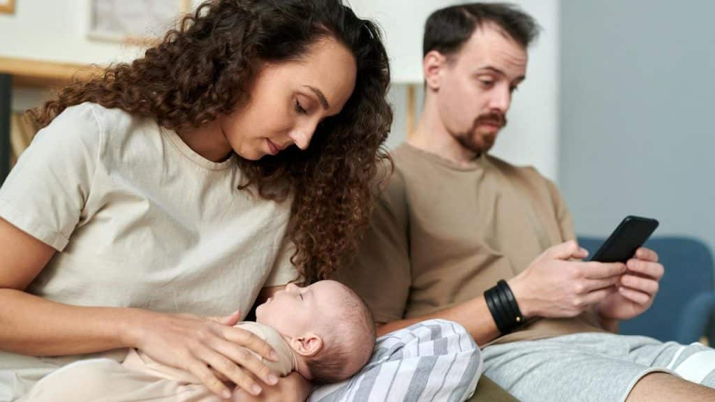 A woman holding a baby while a man beside her looks at his phone