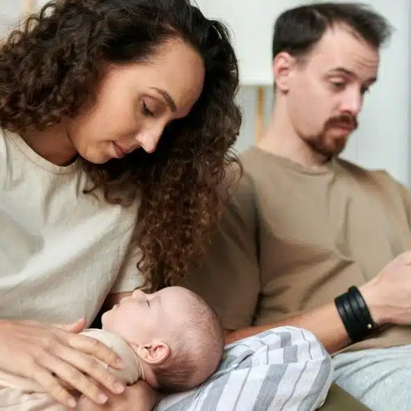 A woman holding a baby while a man beside her looks at his phone