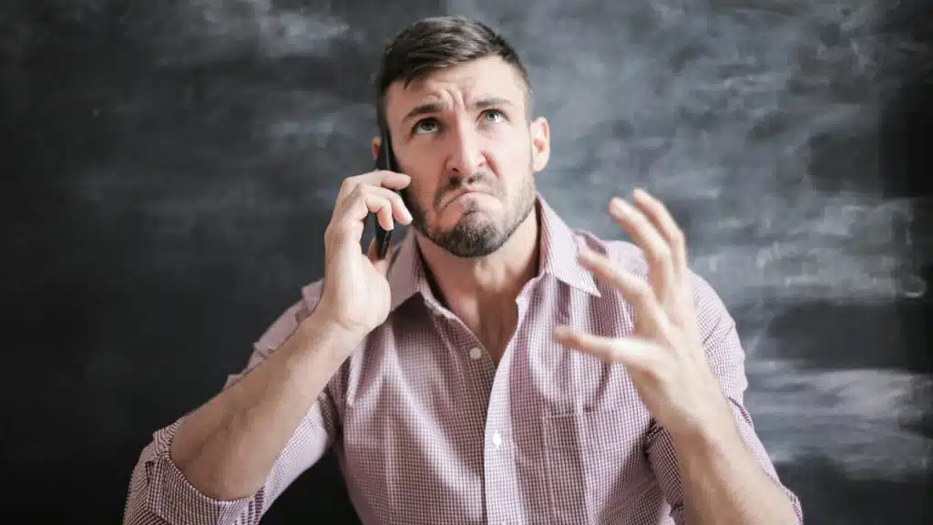 A man in a collared shirt looks annoyed while talking on his mobile phone.