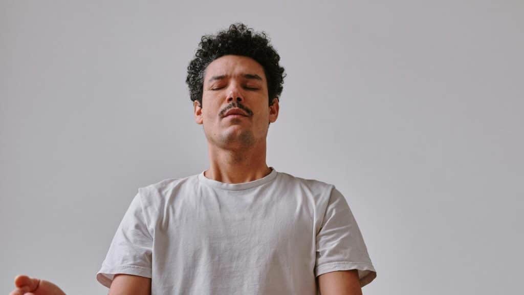A man with closed eyes meditating against a plain background.