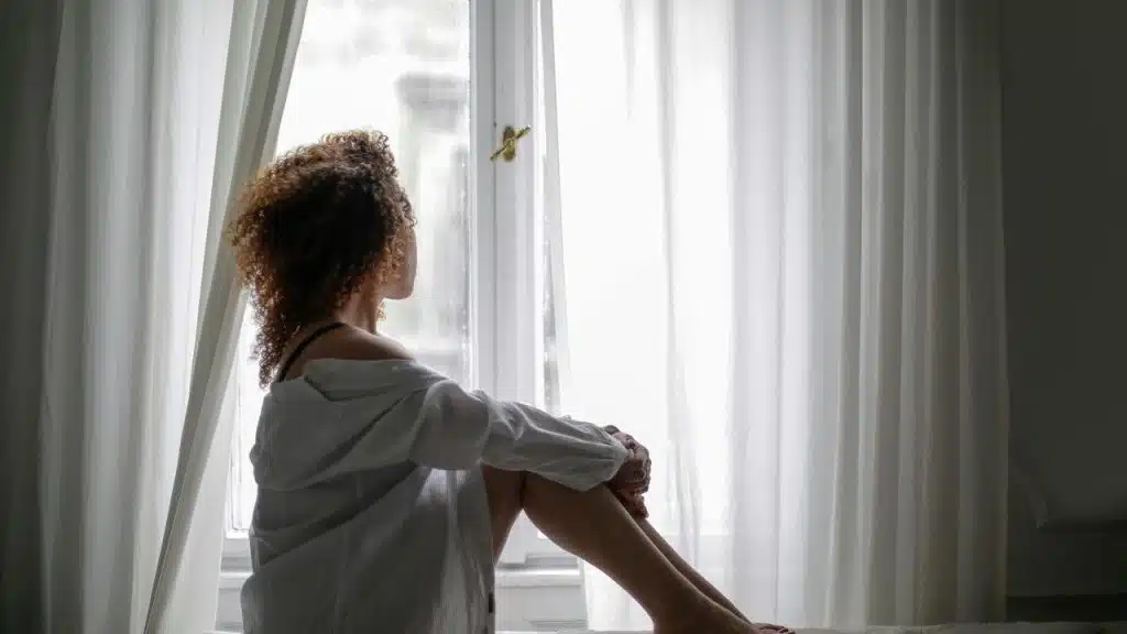 A woman sitting by a window, looking outside.