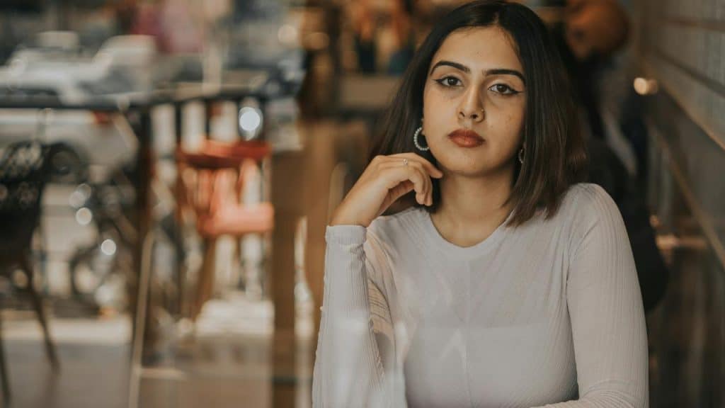 A woman sitting at a café table, resting her chin on her hand and looking ahead.