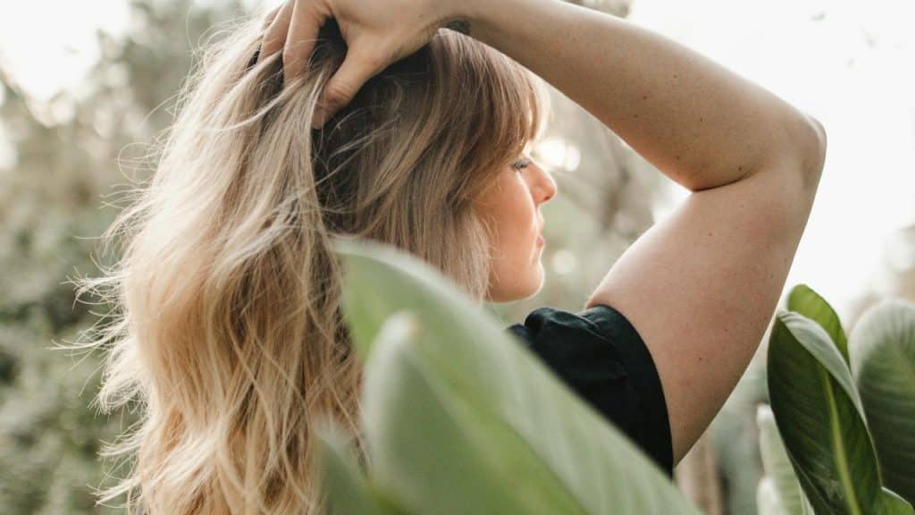 A woman with blonde hair touching her head outdoors