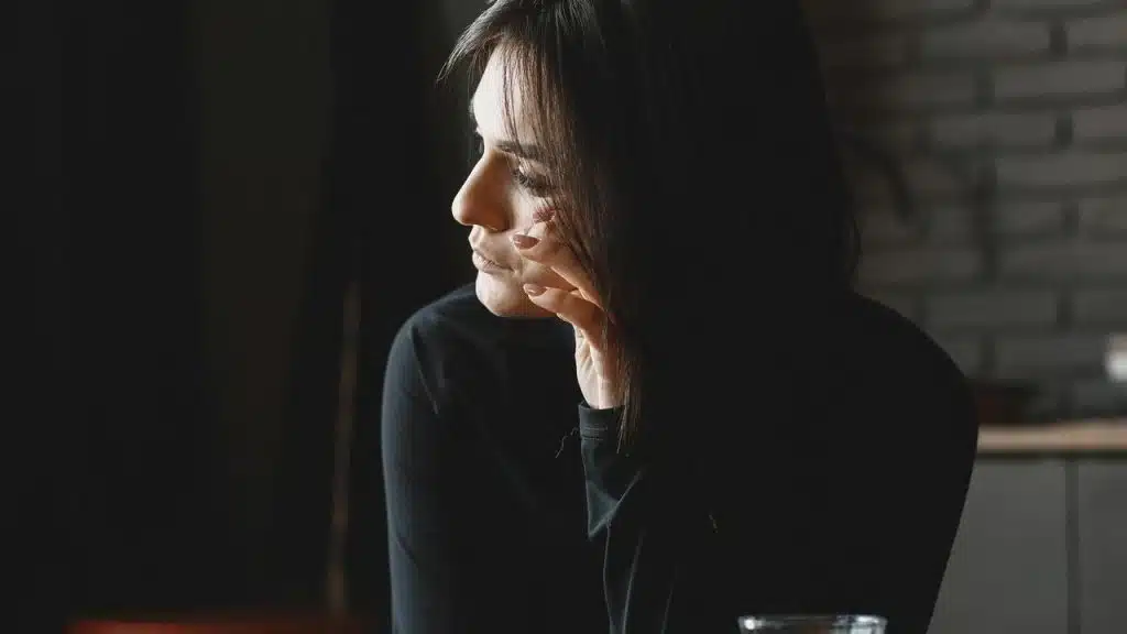 A woman in a dark top resting her head on her hand while gazing out a window.