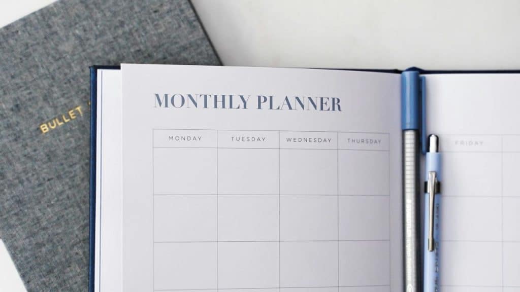 An open monthly planner with blank grid squares sits next to two blue pens.