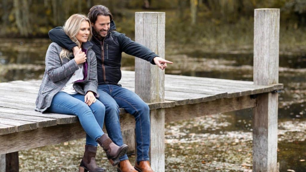 A couple sitting on a wooden dock, with the man pointing ahead.