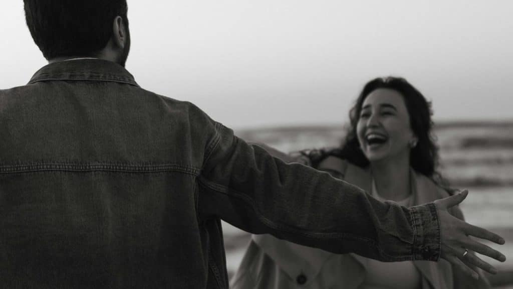 A man with open hands standing in front of a laughing woman who is coming towards him.