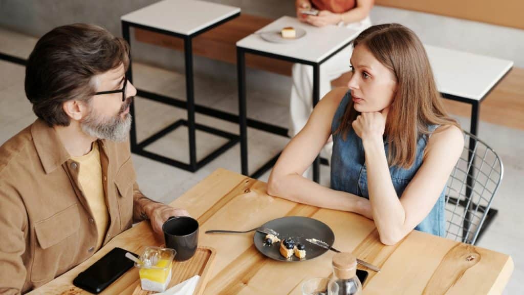 A man and woman sit across from each other at a wooden table in a cafe.