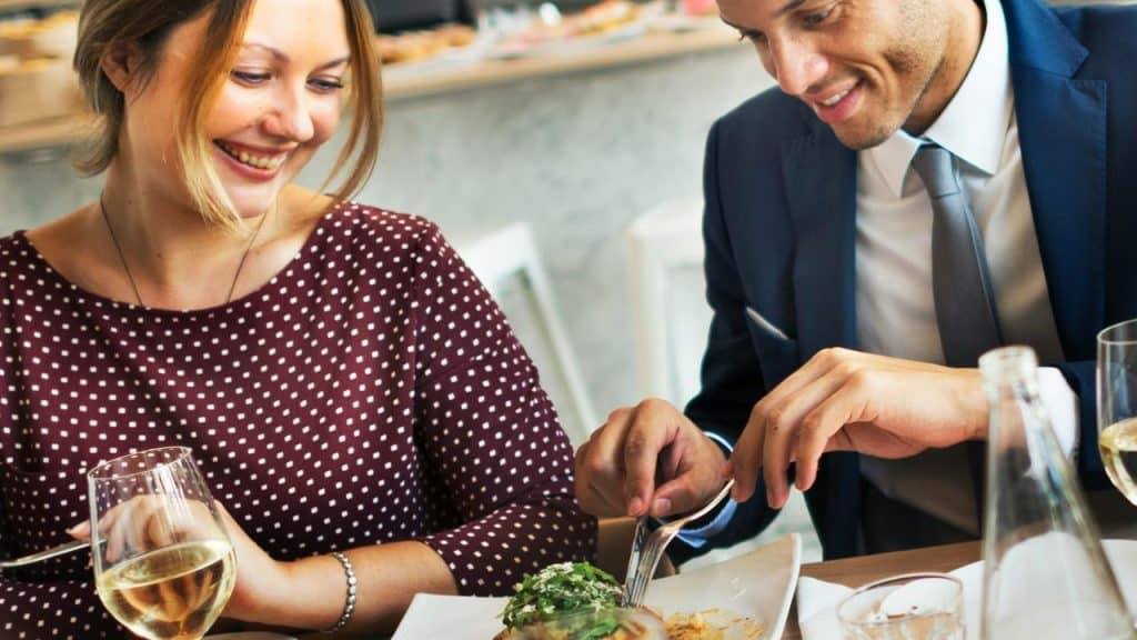 A man and woman smiling while sharing a meal at a restaurant.
