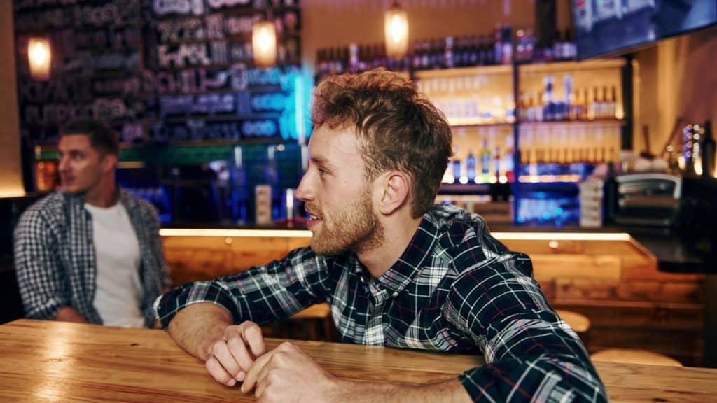 A man sitting at a bar, talking while another person sits nearby.