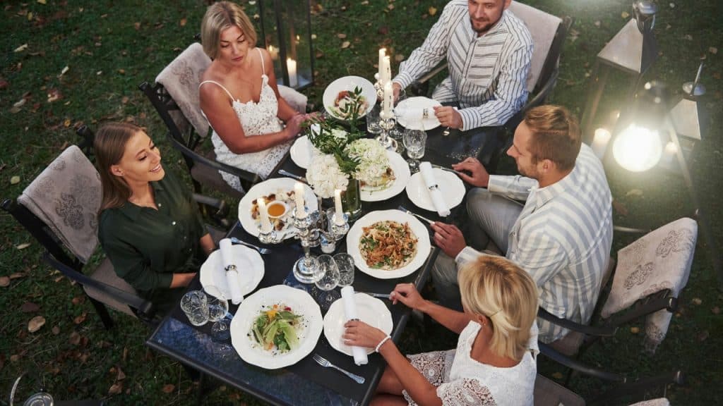 Four people sit around an outdoor table with food and candles at dusk.