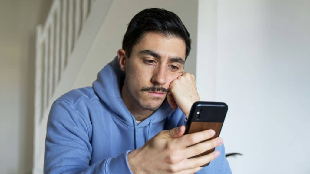 A man in a blue hoodie rests his head on his hand while looking down.
