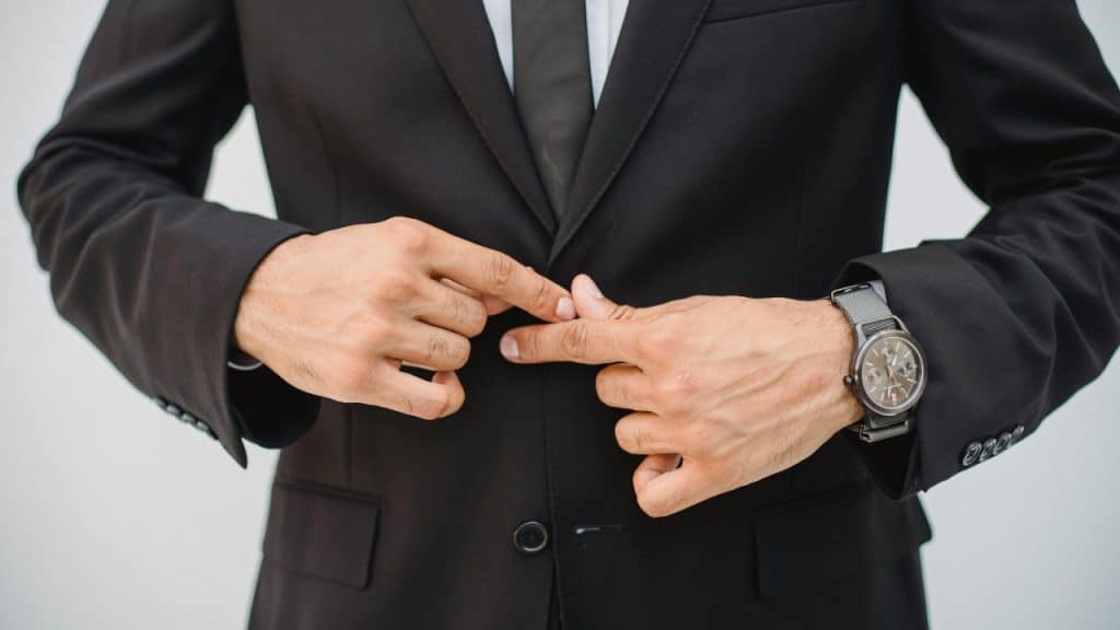 Close-up of a person in a black suit and tie adjusting the buttons on their jacket.