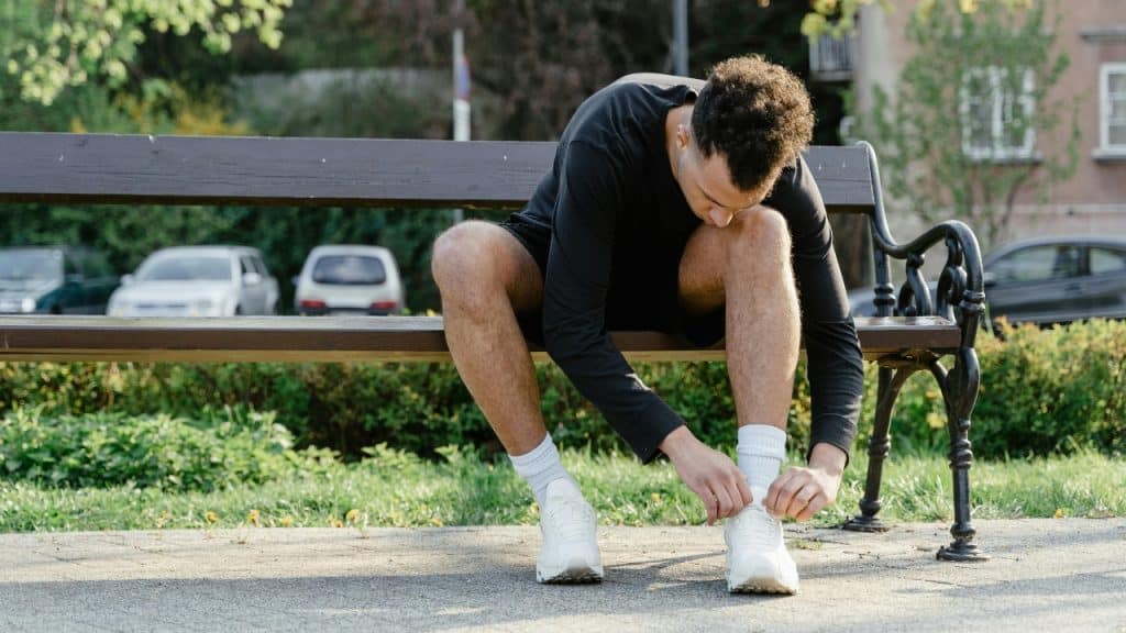 A person in black athletic gear sits on a wooden bench to tie white sneakers.