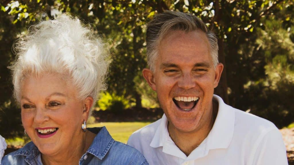 An older couple laughing together under the shade of trees.
