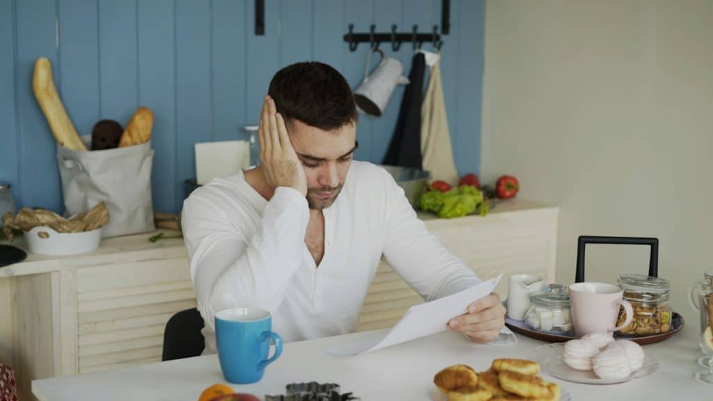 A man sitting at a table reading papers with breakfast.