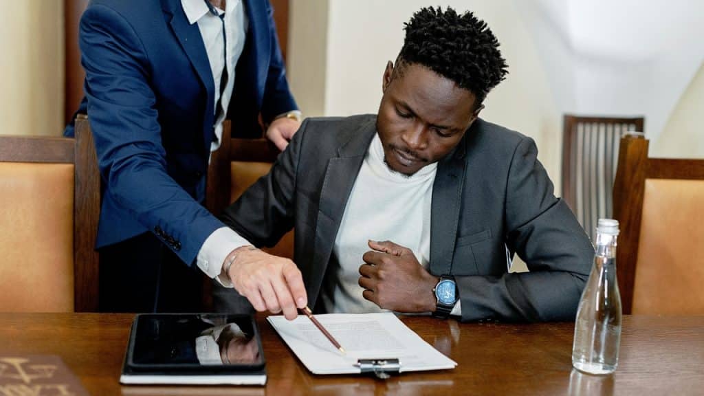A person in a suit points to a document while a man watches.