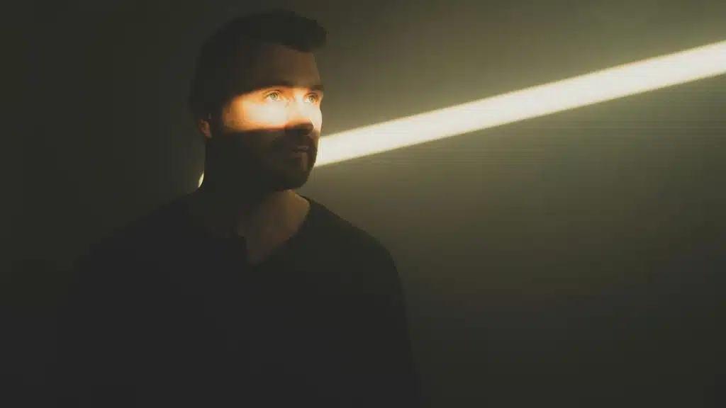 A man standing in shadow with a beam of light crossing his face.