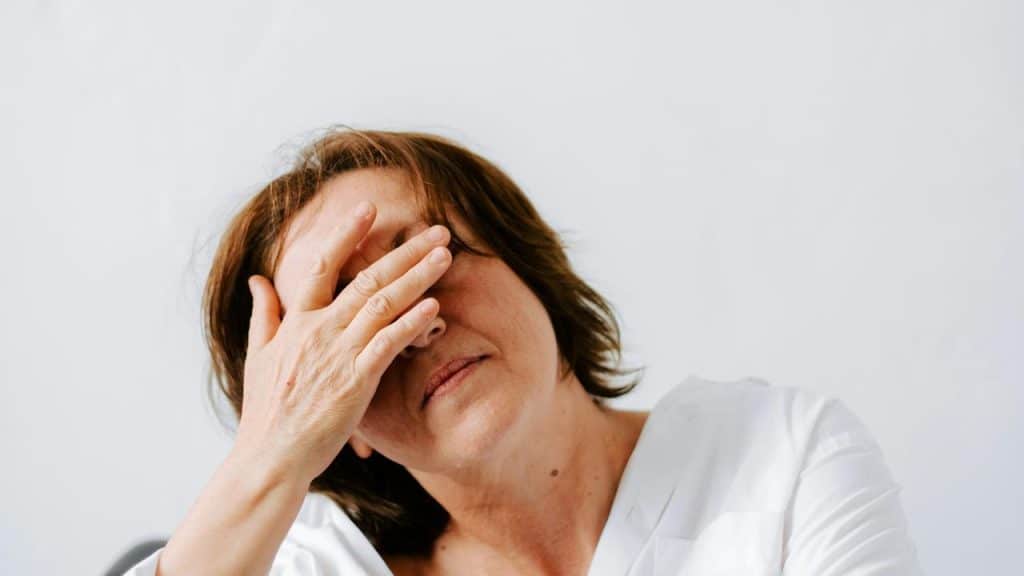 A woman covering her face with her hand against a plain background.