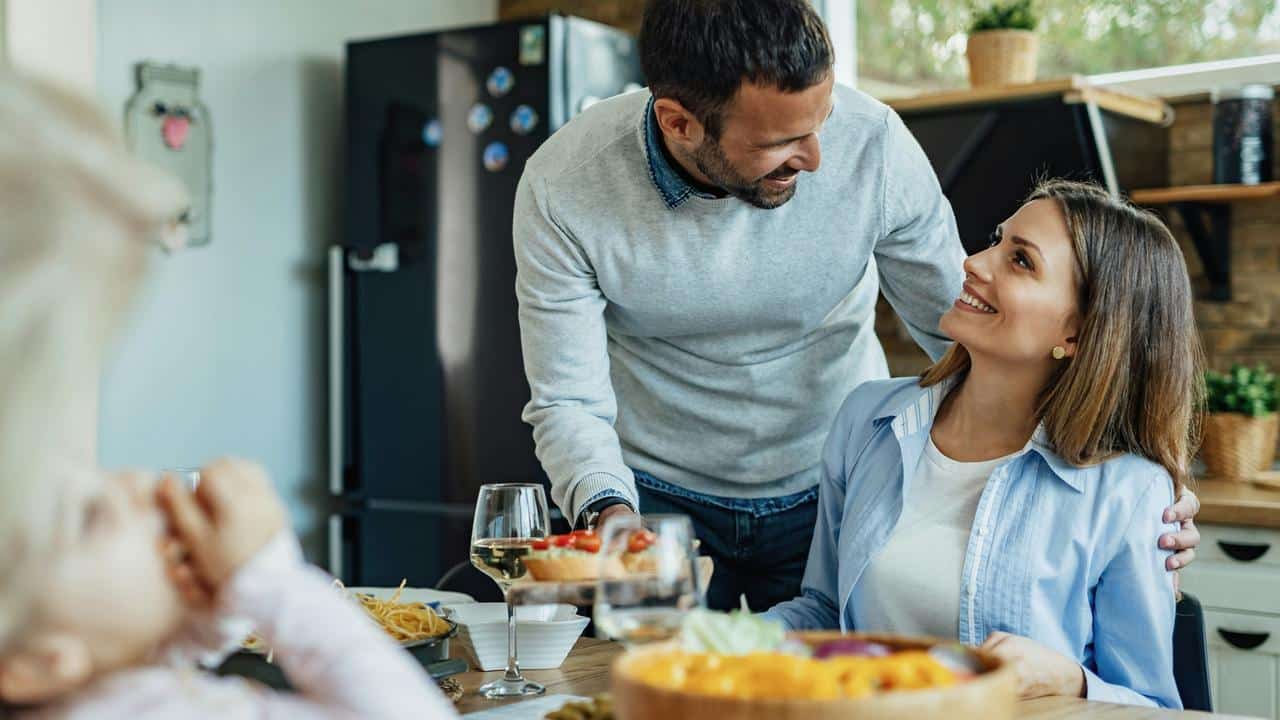 A couple smiling at each other while sharing a meal at home.