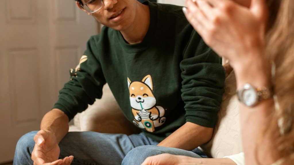 A person talking with another person while sitting on a couch indoors.