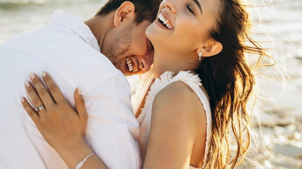 A couple embracing and smiling on a sunny beach.