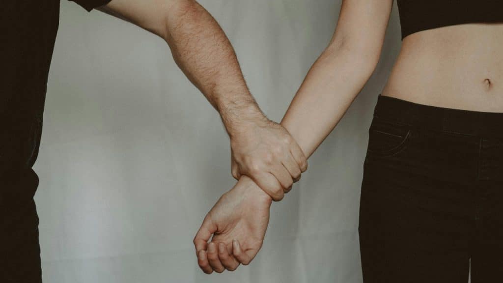 A person is firmly holding another person's wrist against a plain background.