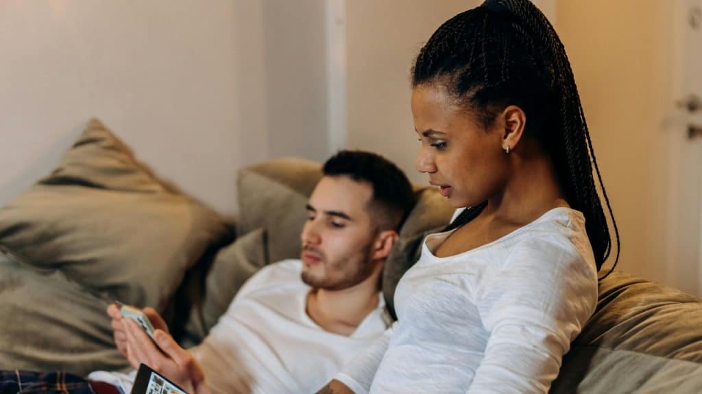 A woman with braided hair looks at a device while a man uses his phone.