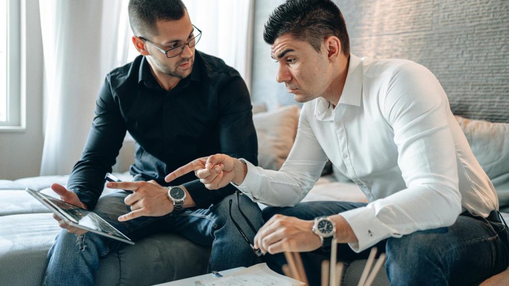 A pair of men sitting together and reviewing financial charts on a tablet.