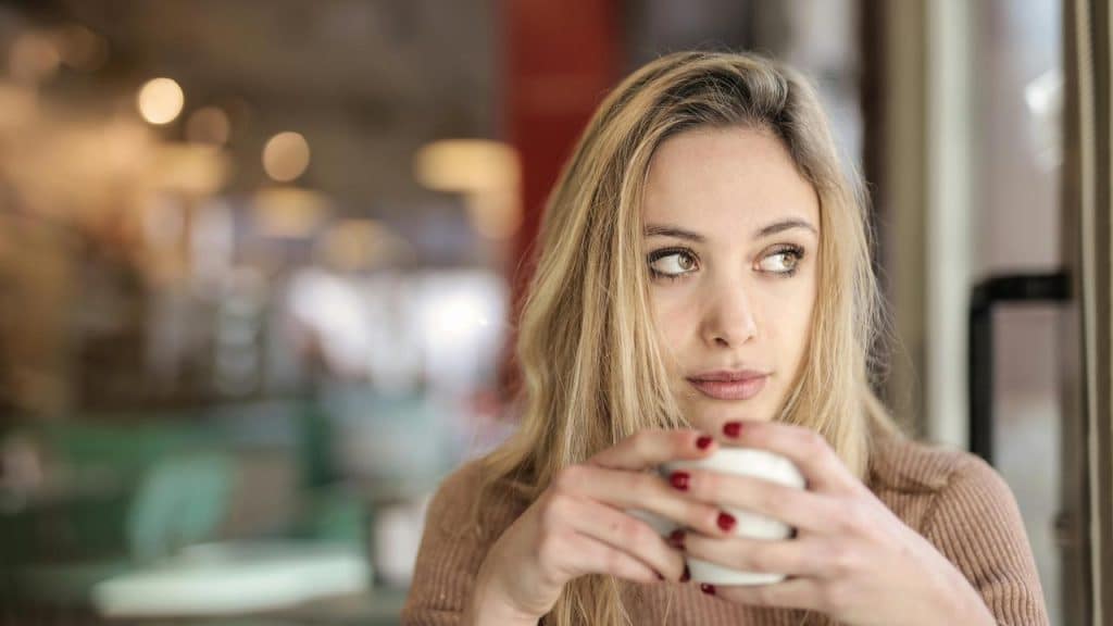 A woman holding a cup and looking away while sitting in a café.